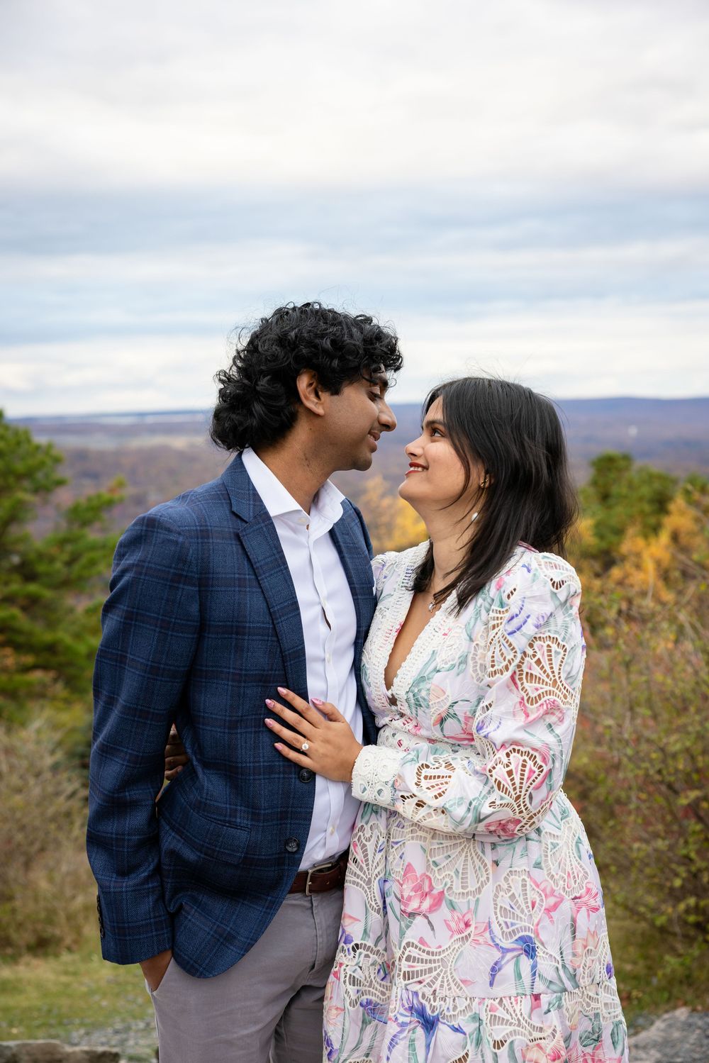 Couple in elegant attire smiling at each other on scenic autumn overlook.