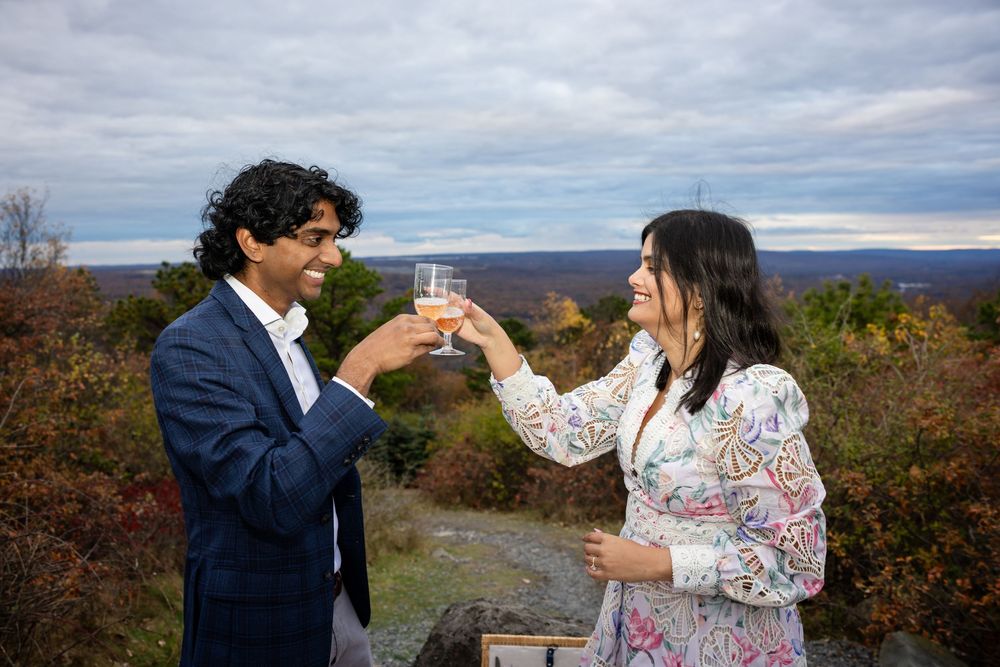 Happy couple toasting with champagne glasses on scenic mountain overlook in fall.