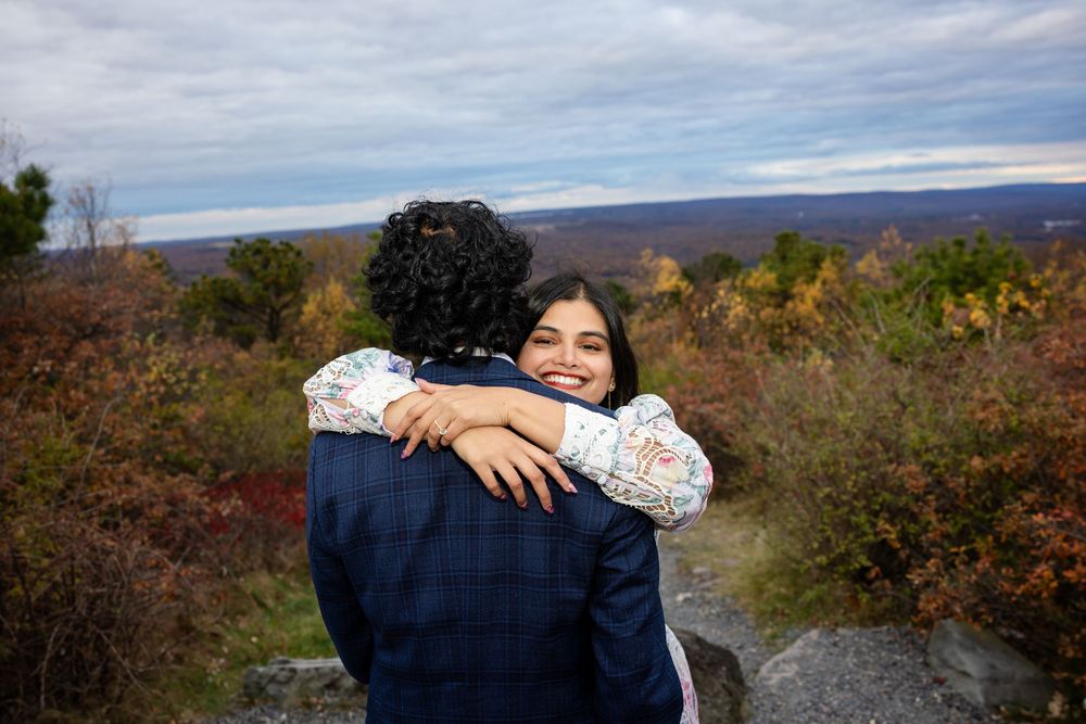 Happy woman smiling while hugging her partner at a scenic autumn overlook with colorful fall foliage.