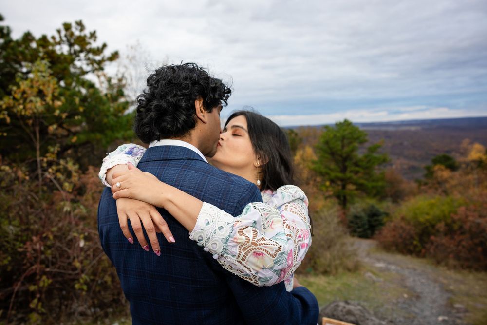 Couple sharing a romantic kiss at a mountain overlook surrounded by vibrant autumn foliage.