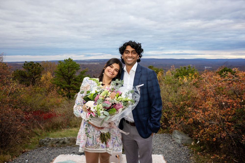 Smiling couple posing together at a mountain overlook, woman holding a beautiful pink and white bouquet.