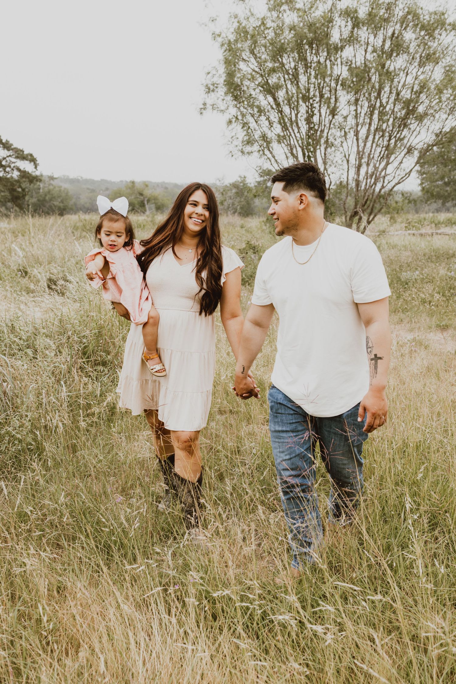 A family in white outfits walks together through a sun-drenched field of tall grass on a summer afternoon.