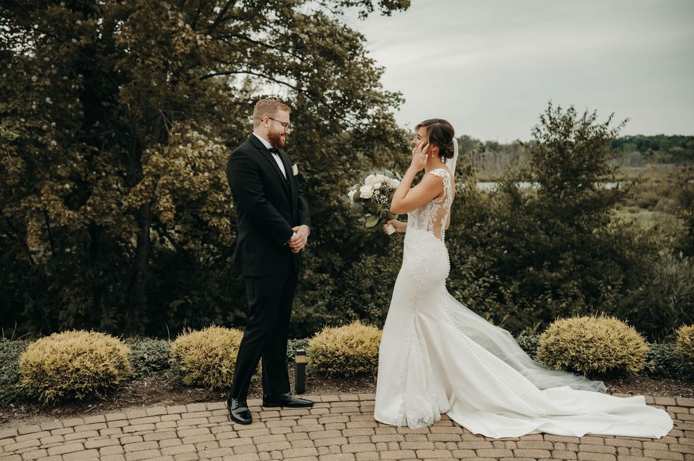 Groom's emotional reaction seeing bride in lace wedding gown during outdoor first look.