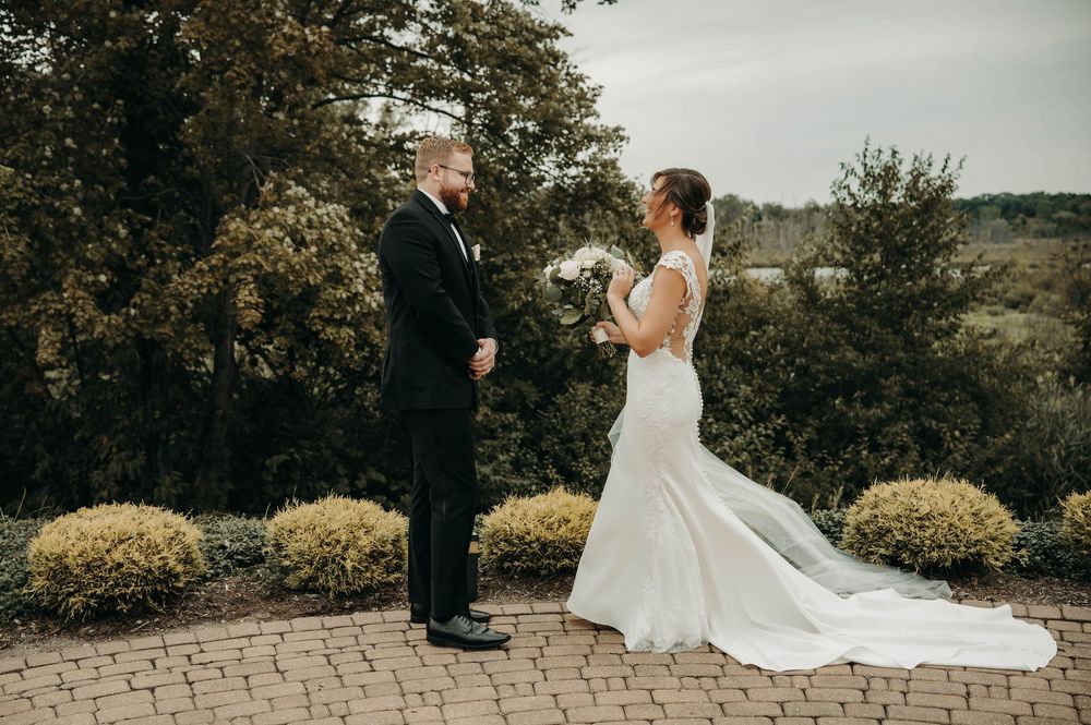 Bride and groom sharing first look moment on brick terrace with scenic garden backdrop.