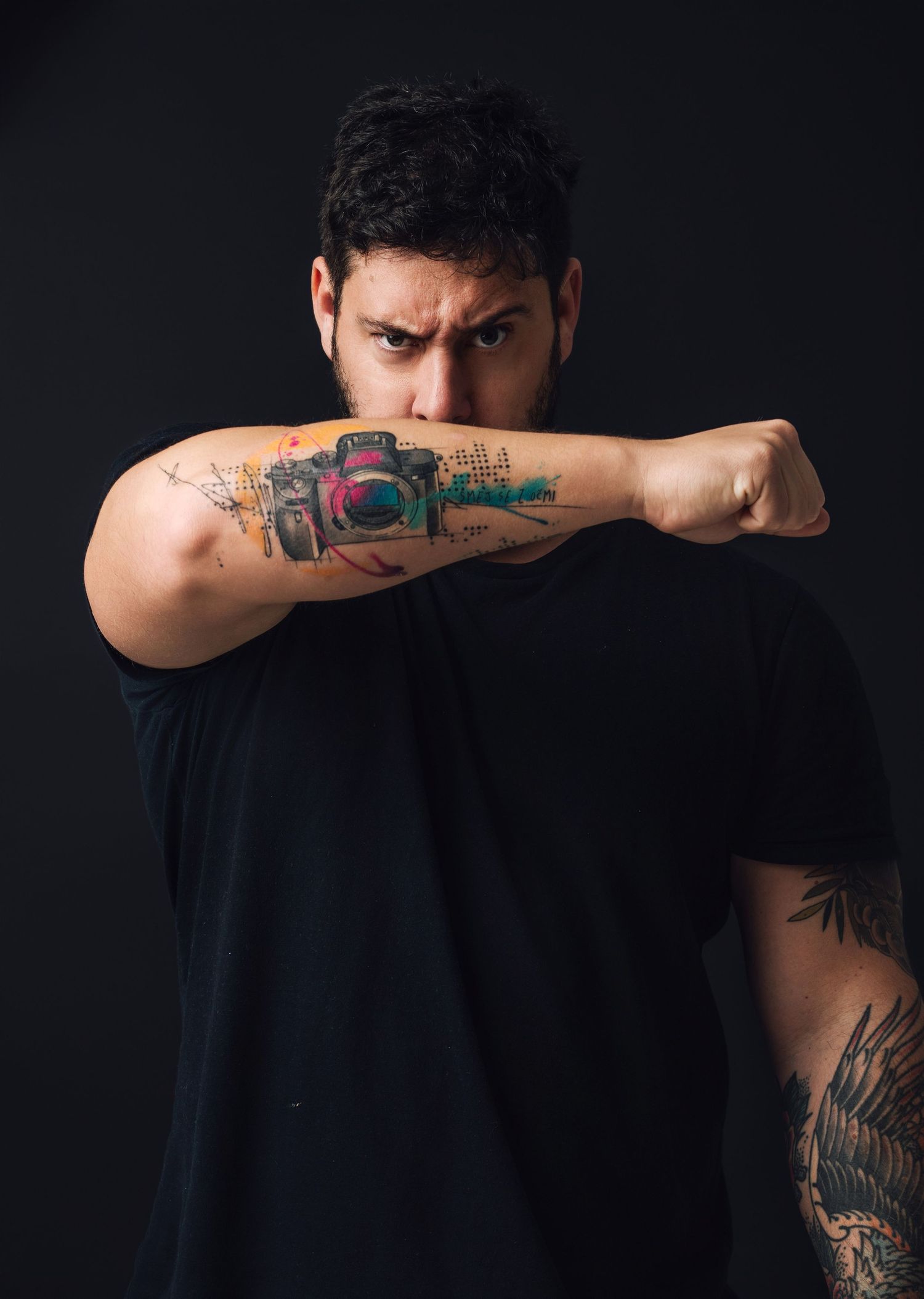 Artistic tattoo of a camera design displayed on person's forearm against black background.