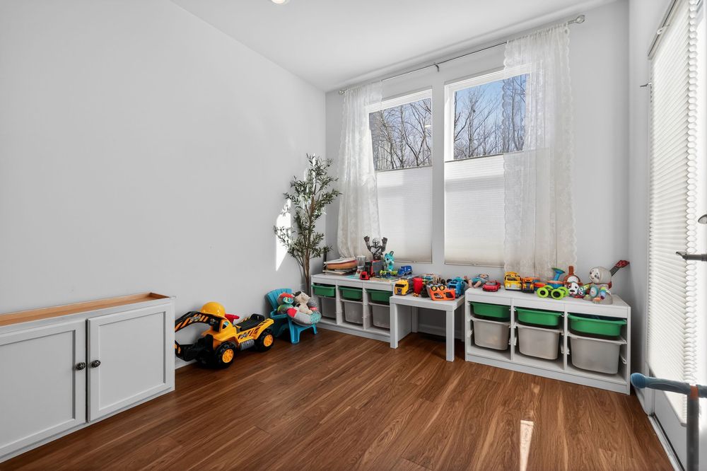 Bright children's playroom with hardwood floors, toy storage bins, and a large window with sheer curtains.