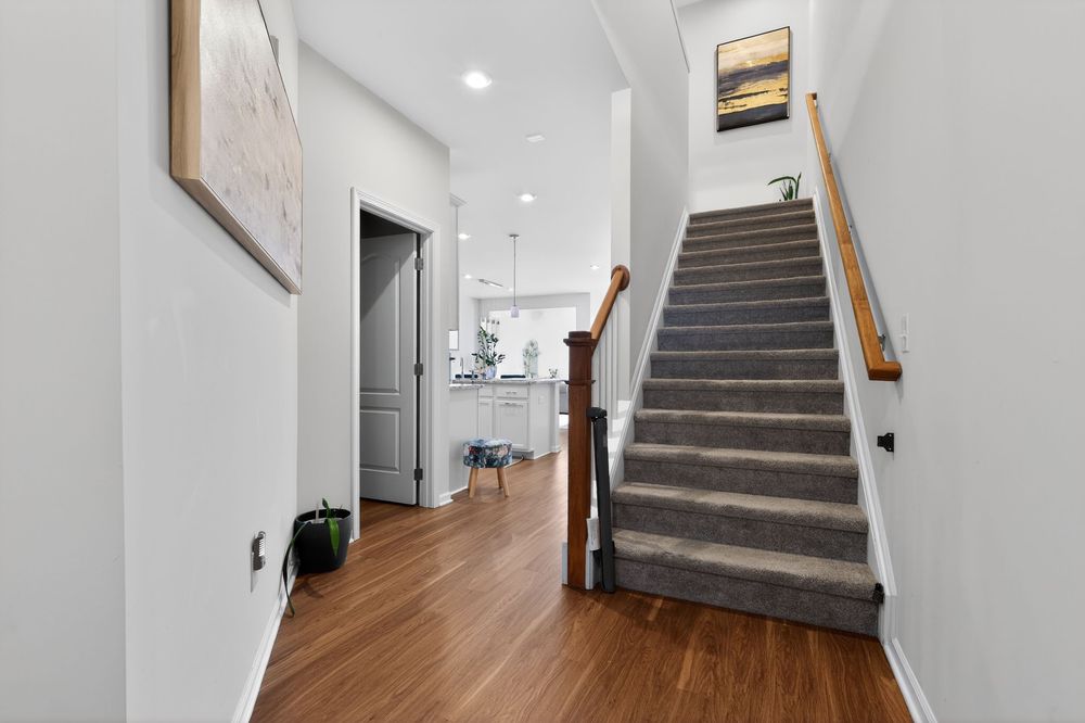 Welcoming entryway with hardwood floors, carpeted staircase with wood railing, and view to kitchen.