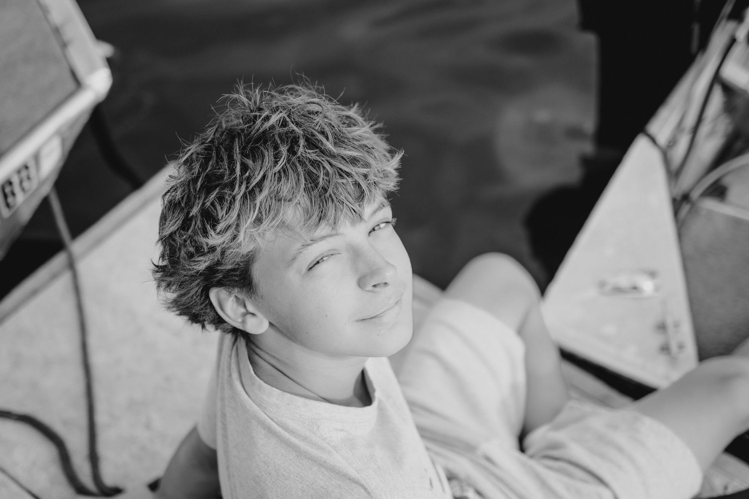 Black and white portrait of a young boy with wet curly hair relaxing on a boat with eyes closed.