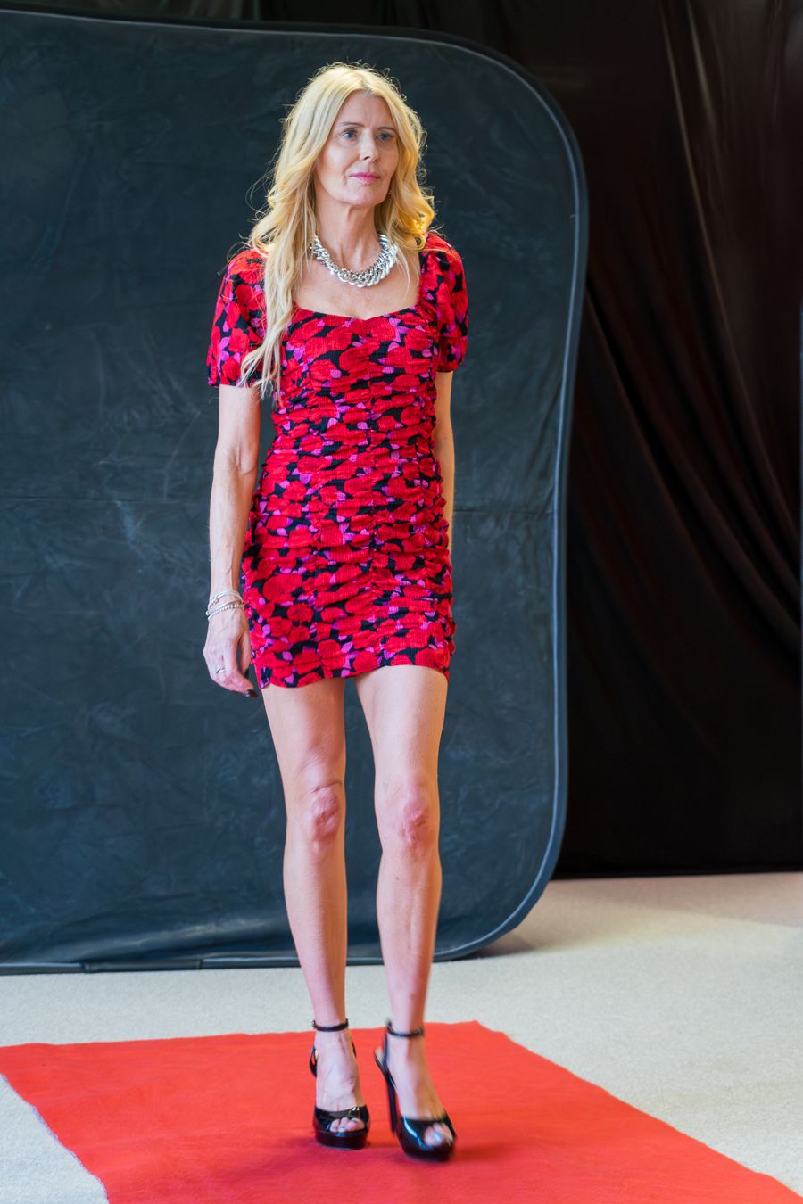 Model poses on red carpet wearing a vibrant red and black patterned mini dress with black pumps.