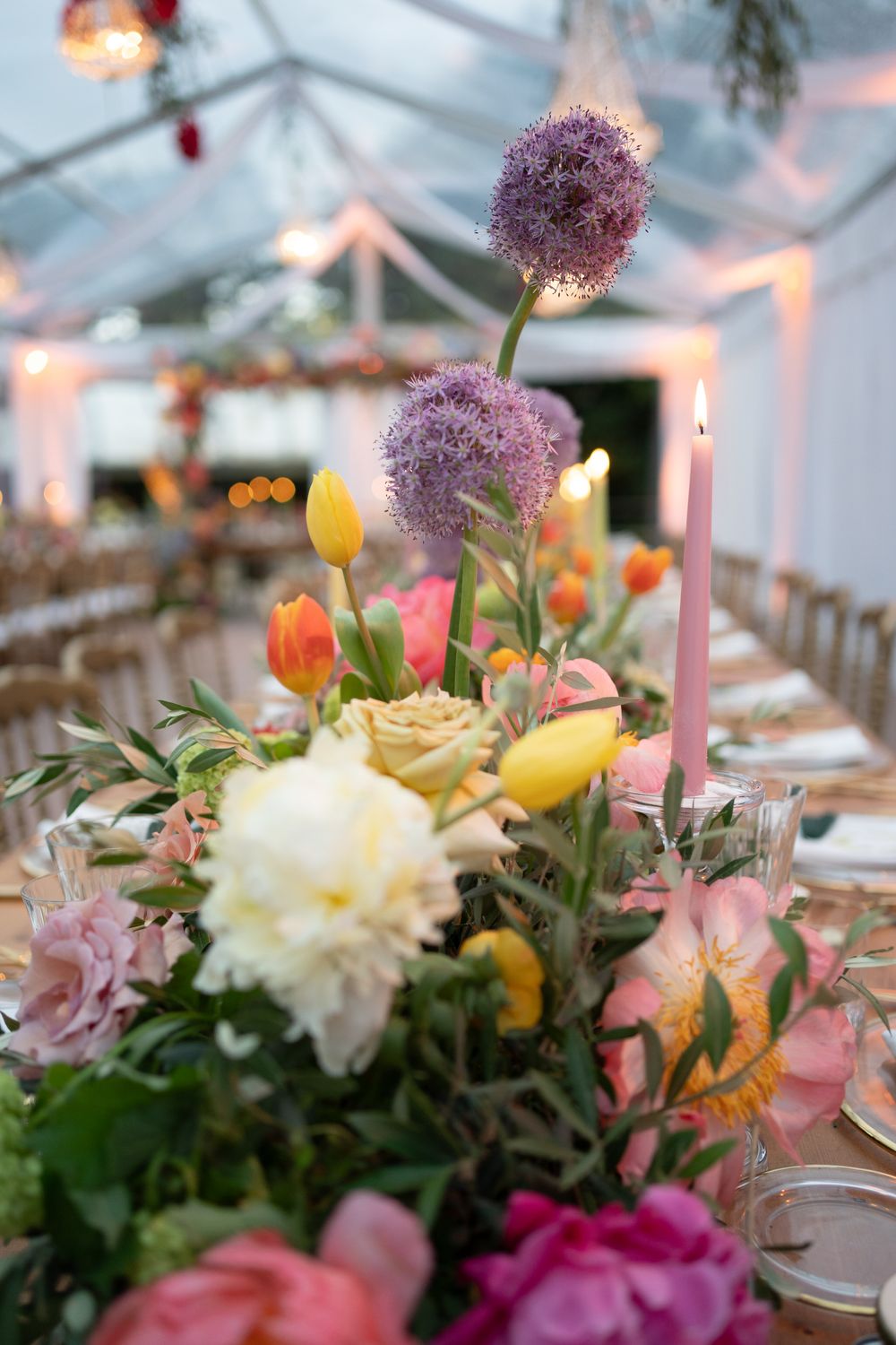 Elegant wedding table centerpiece featuring pink and white flowers with glowing candles under a white tent.