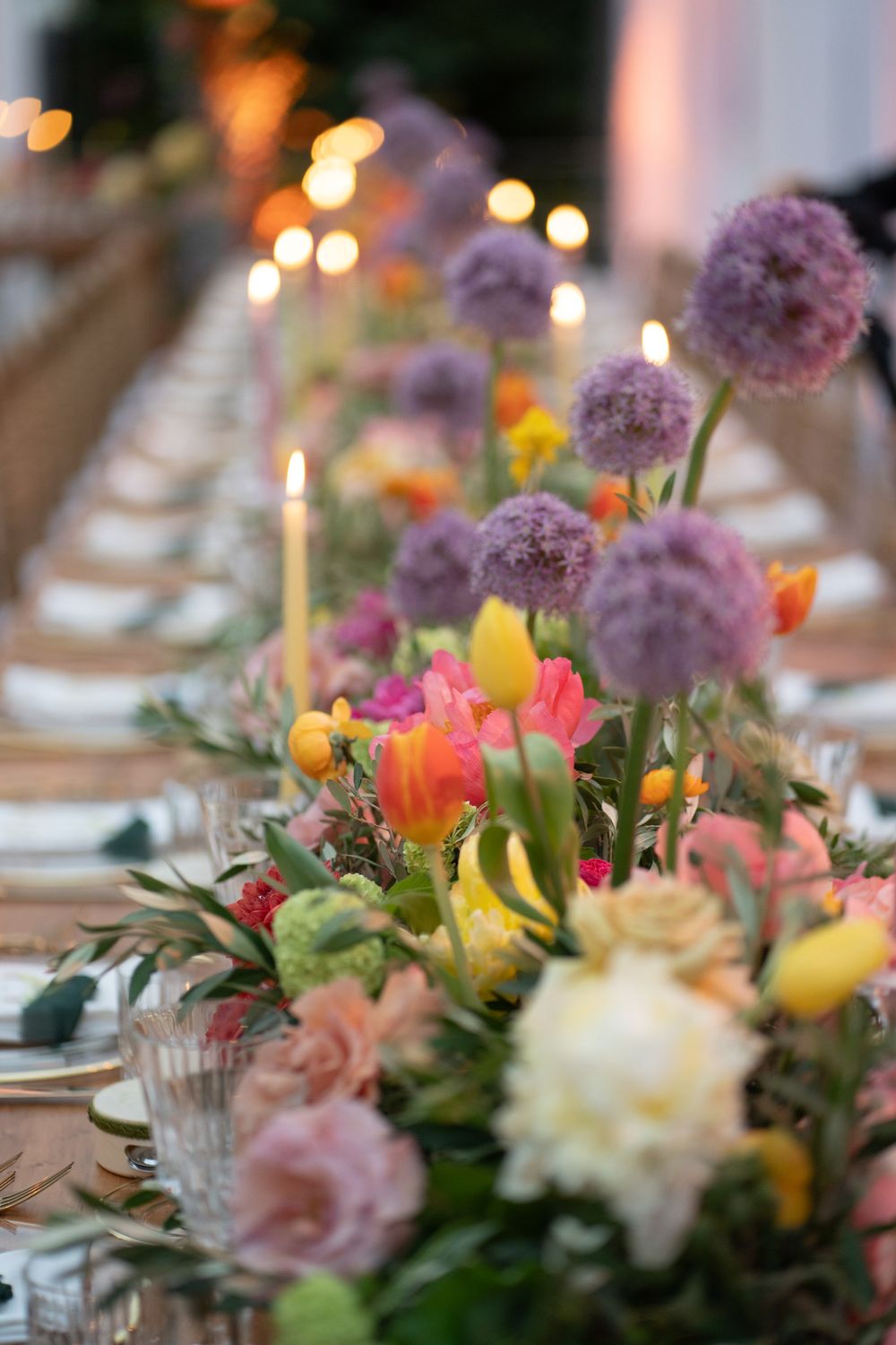 Elegant table setting with colorful floral centerpieces featuring pink, purple and yellow blooms illuminated by soft candlelight.