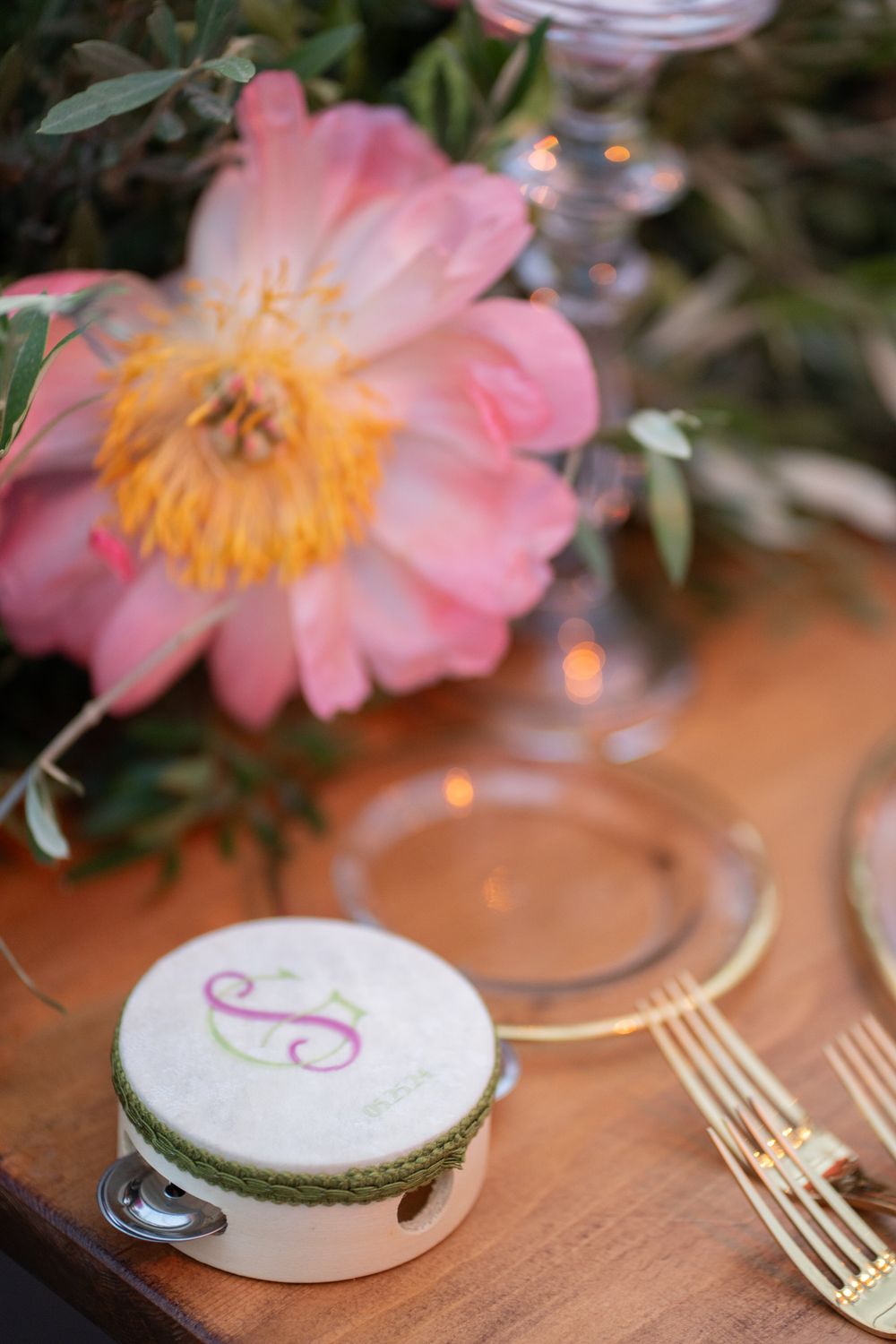 Close-up of pink flowers and gold flatware next to personalized place cards on a wooden table.