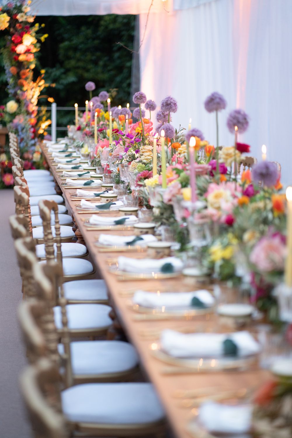 Elegant wedding reception table setting with white plates and colorful floral centerpieces arranged in a long row.