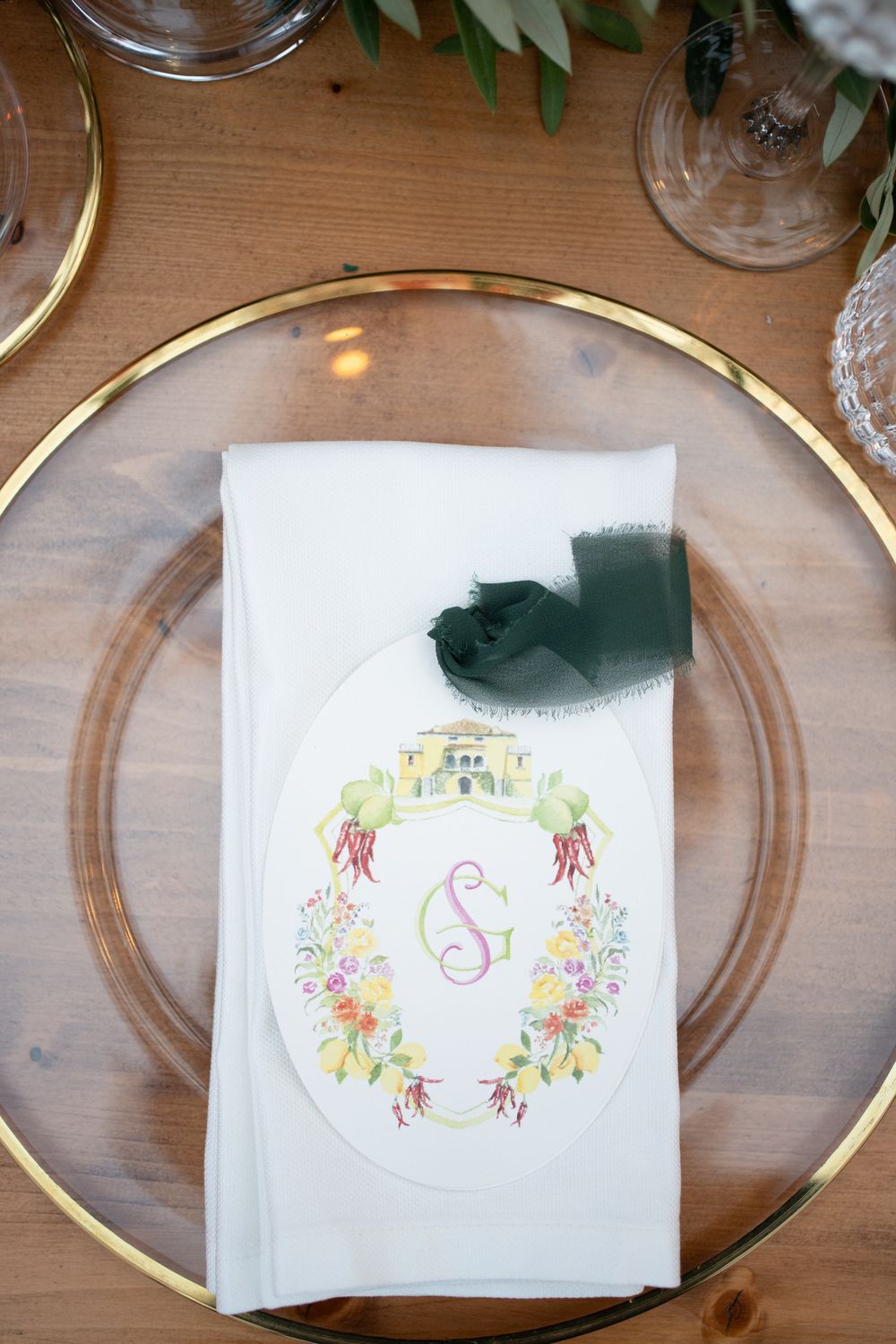 Wedding place settings with custom monogrammed floral paper napkins and gold-rimmed glass charger plates.