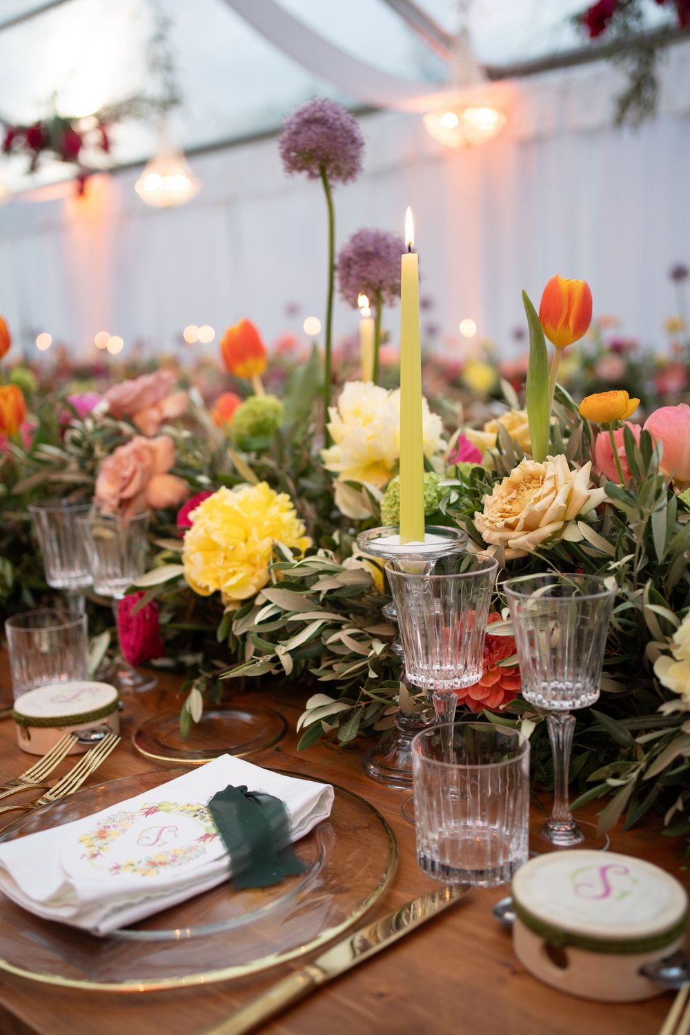 Elegant table setting with crystal glasses, candles, and colorful floral arrangements featuring tulips and roses on a wooden table.