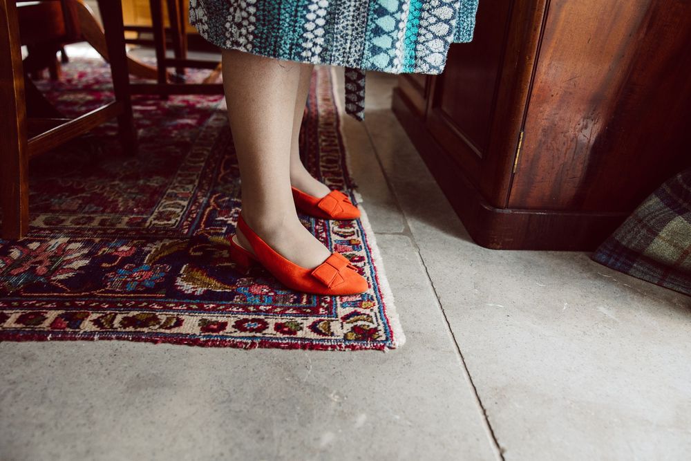 Close-up view of orange heels walking on a decorative carpet in a dimly lit room.