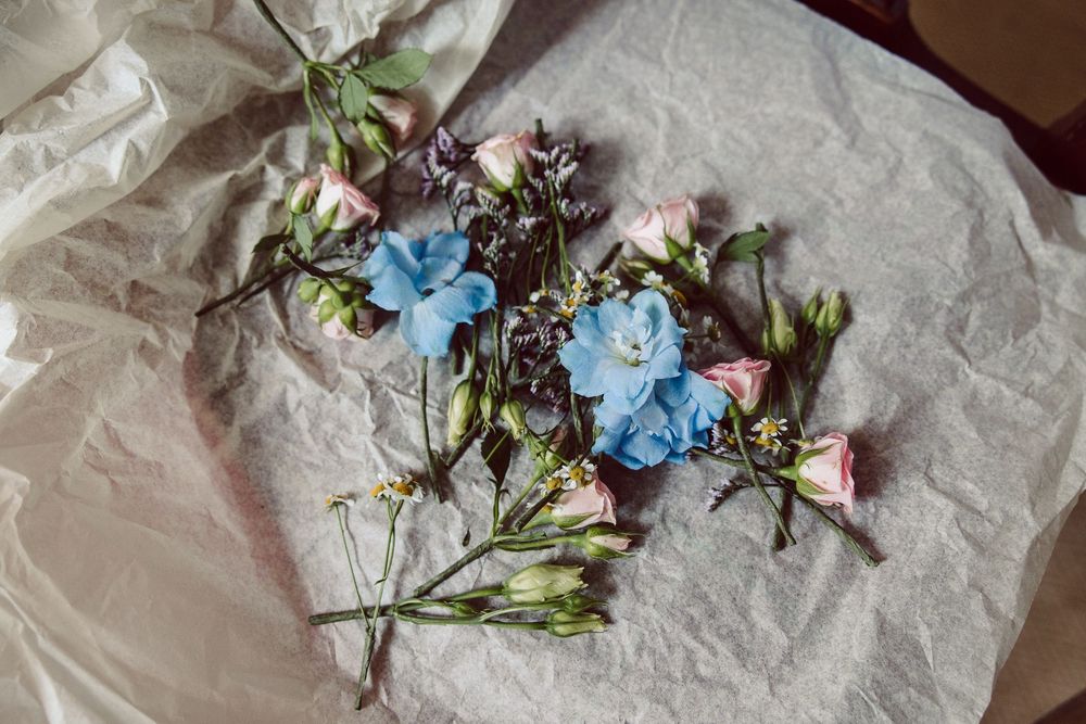 Delicate blue and pink flowers arranged on crumpled white paper with scattered petals creating a romantic composition.