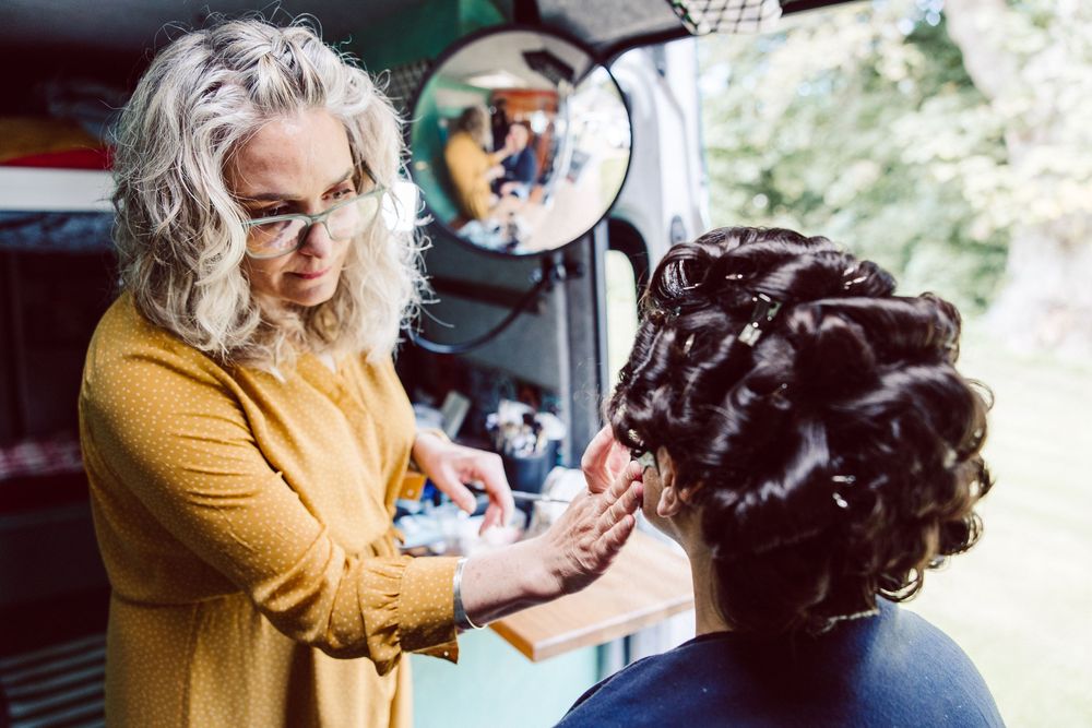 A hairstylist in a yellow cardigan carefully styles dark curly hair in a professional salon setting.