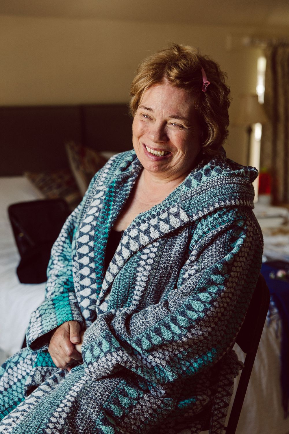 Person wearing a cozy blue and gray patterned knit cardigan smiles warmly while sitting on furniture at home.