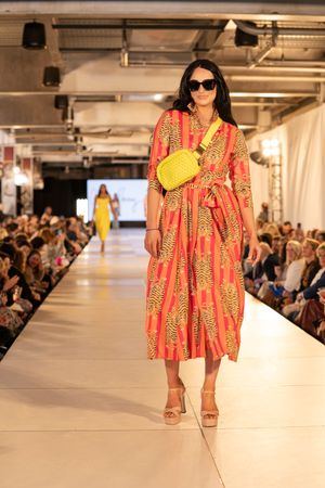 Model showcasing vibrant red and yellow patterned summer dress with yellow handbag on fashion runway.