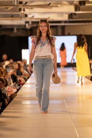 Models showcase casual denim looks on a brightly lit runway at a fashion show.