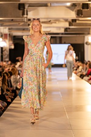 Floral print babydoll dress being showcased on brightly lit catwalk with audience in background.