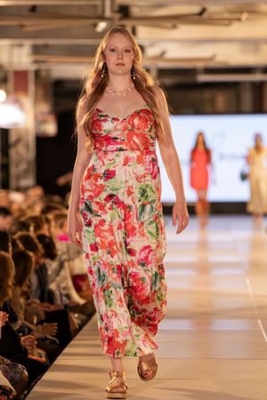 Bright floral print summer dress displayed during fashion show with audience seated along runway.