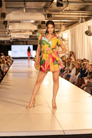 Models showcase vibrant tropical print fashion designs on a white runway during a fashion show.
