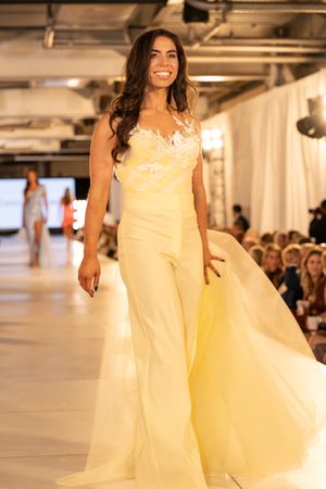 Flowing pale yellow evening gown with delicate details showcased on illuminated catwalk.