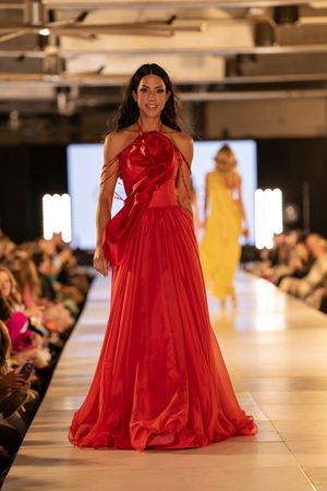 Dramatic red ballgown with full skirt flows across fashion runway.