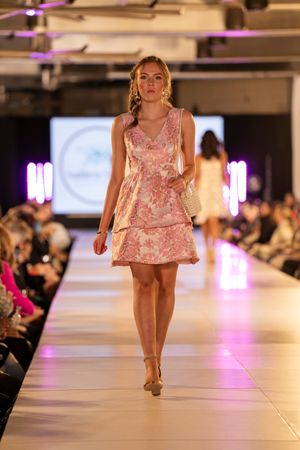 Short pink cocktail dress with ruffled details displayed on illuminated fashion runway.