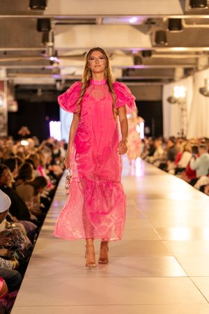 Bright pink ruffled dresses showcased on illuminated catwalk at fashion event.