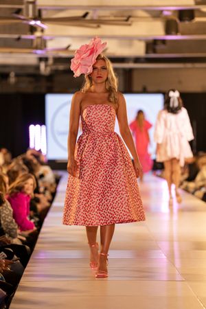 Model presents red and white patterned summer dress on brightly lit catwalk.