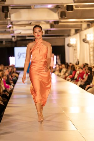 Elegant peach-colored evening wear displayed on illuminated runway at fashion show.