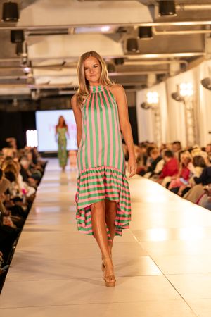 Striped green and white summer dress flows down illuminated catwalk.