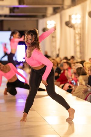 Dancers in black leggings perform contemporary dance moves on a light colored floor in a studio with warm lighting.