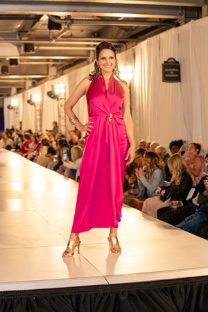 Model struts down catwalk in vibrant hot pink dress during evening fashion show.