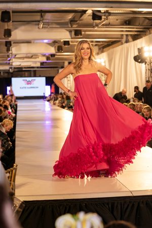 Flowing red gown with dramatic ruffled hem swirls on catwalk during fashion show.