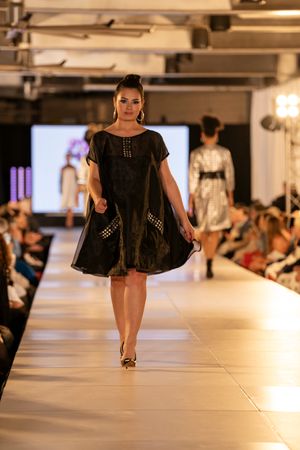 Models present black cocktail dresses while walking down an illuminated fashion show runway.