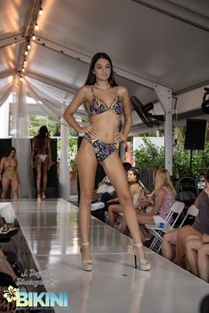 Model walks runway in patterned swimwear during outdoor fashion event.