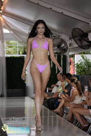 Models display pink bikini designs during a summer fashion show under a white canopy.