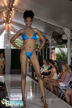 Swimwear models present bright blue bikinis on an outdoor covered catwalk.