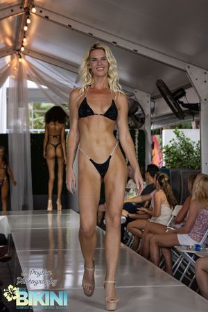 Models walk the catwalk in black swimwear during a summer fashion presentation.