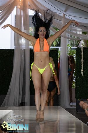 Models display neon yellow and orange bikinis on a covered outdoor catwalk.