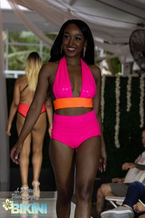 Models walk the runway in vibrant pink and orange swimwear at a beachwear fashion show.
