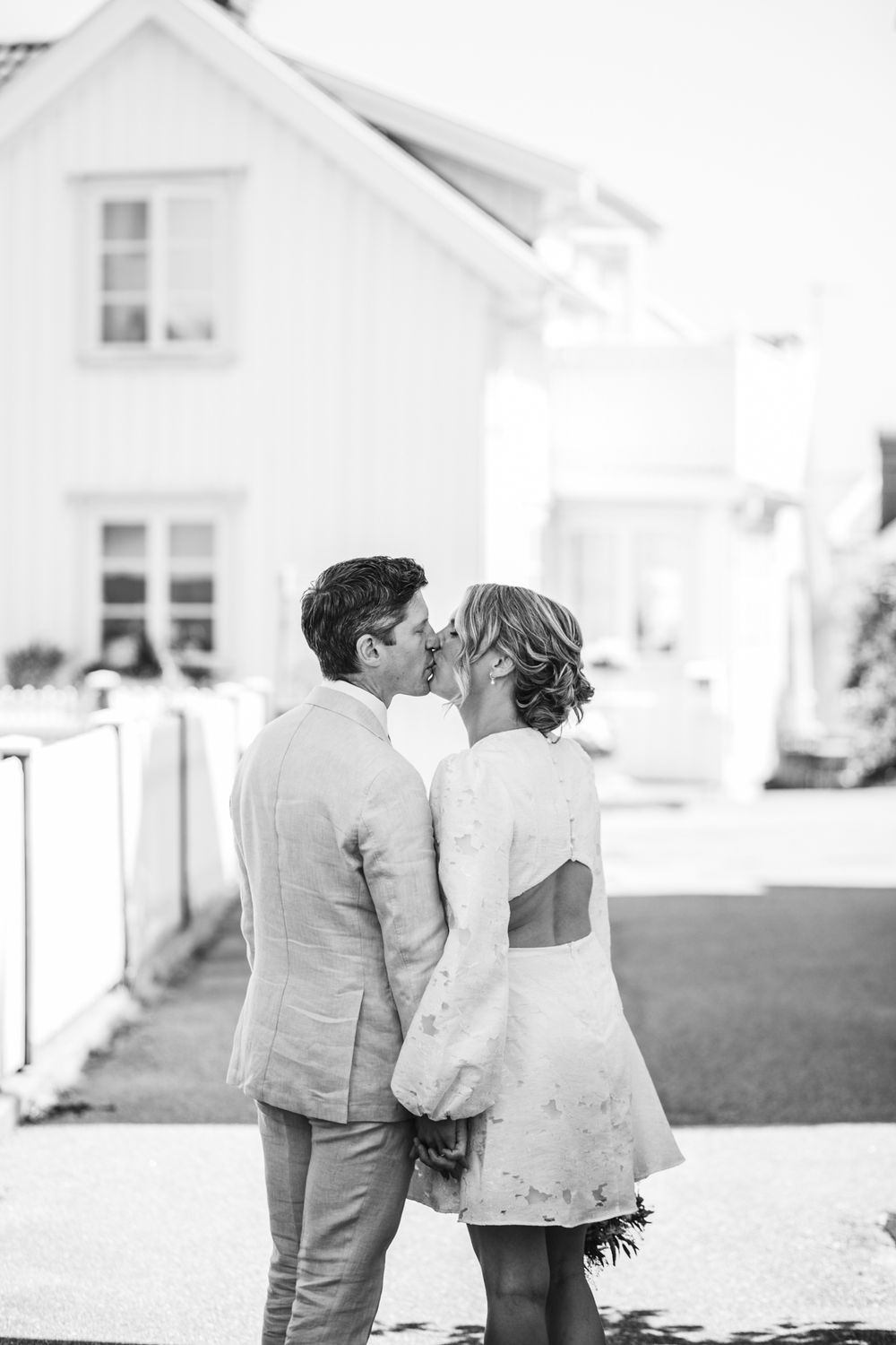 A couple in wedding attire walks together on a path with white buildings in the background.