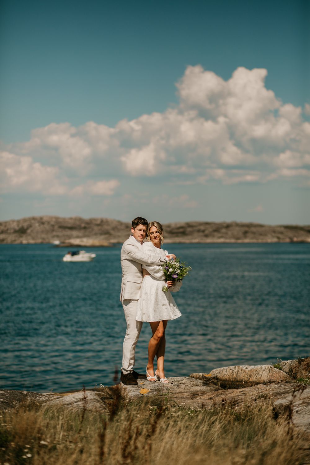 A romantic seaside wedding photoshoot with a couple in white standing on rocky cliffs overlooking turquoise waters.