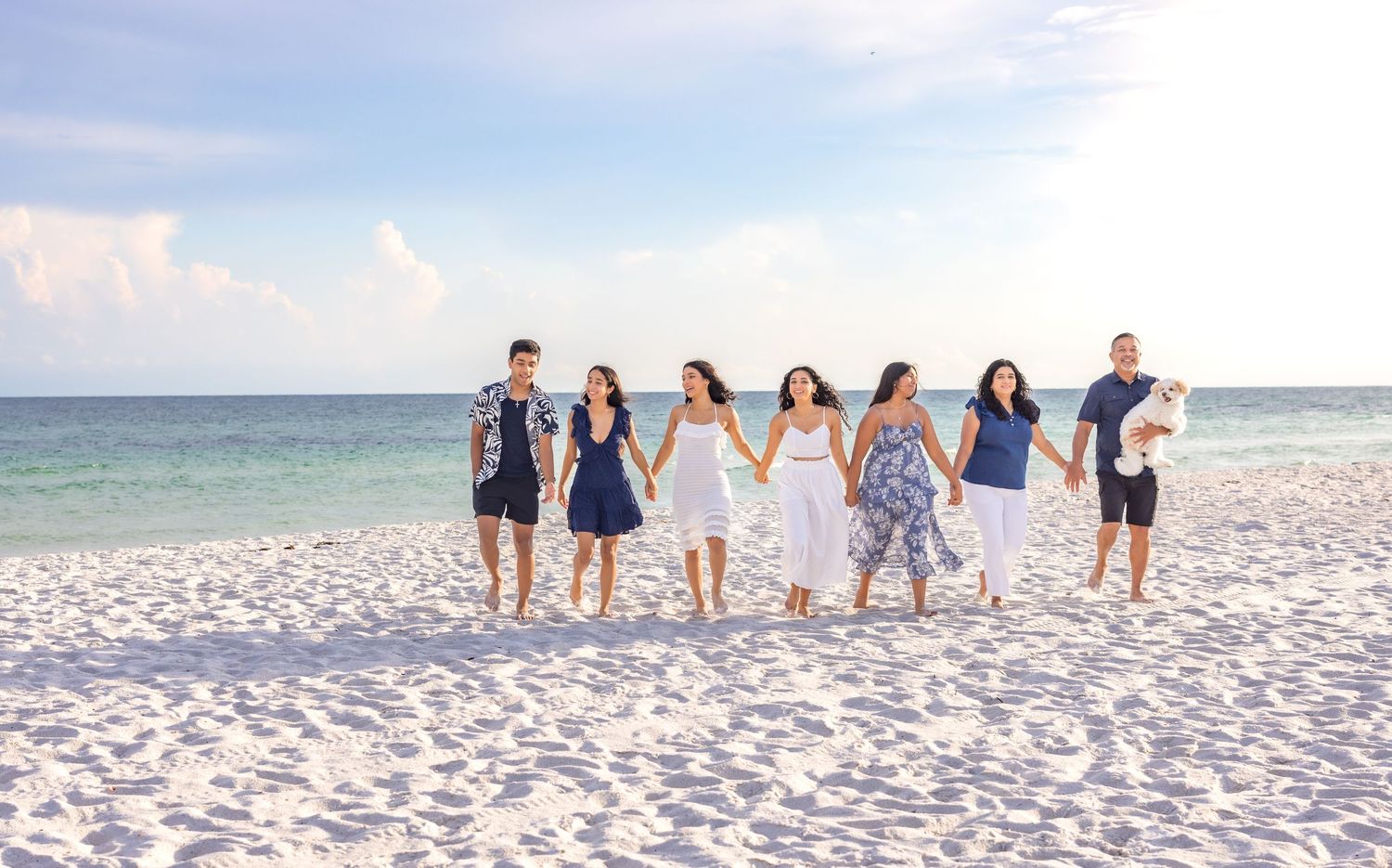 A group of people wearing blue and white outfits pose together on a pristine white sand beach.