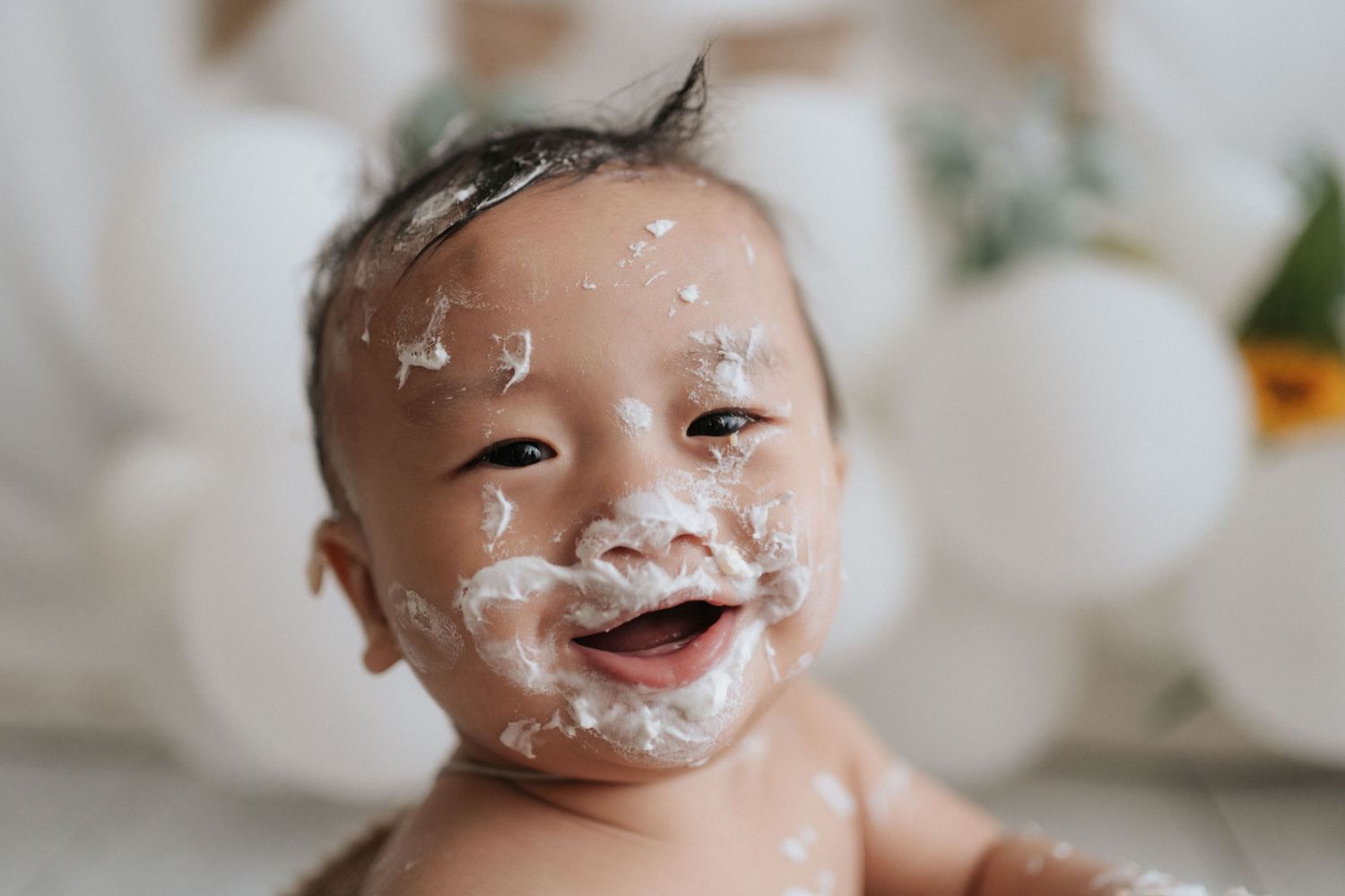 A small child laughs while covered in white cream or lotion on their face during a messy playtime moment.