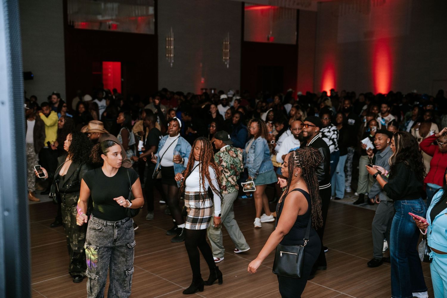 Large crowd gathering in dimly lit indoor space with red ambient lighting.